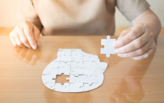 Elderly woman hands holding missing white jigsaw puzzle piece down into the place as a human head brain shape. Creative idea for memory loss, dementia, Alzheimer's disease and mental health concept.