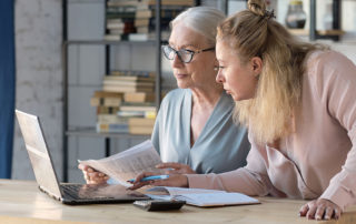 Senior woman using laptop for websurfing in her kitchen. middle-aged daughter helps her mother with documents. Mature lady sitting at work typing a notebook computer in an home office